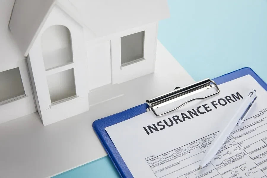 Home insurance application form on a clipboard beside a white house model, representing flood coverage required for a Florida mortgage