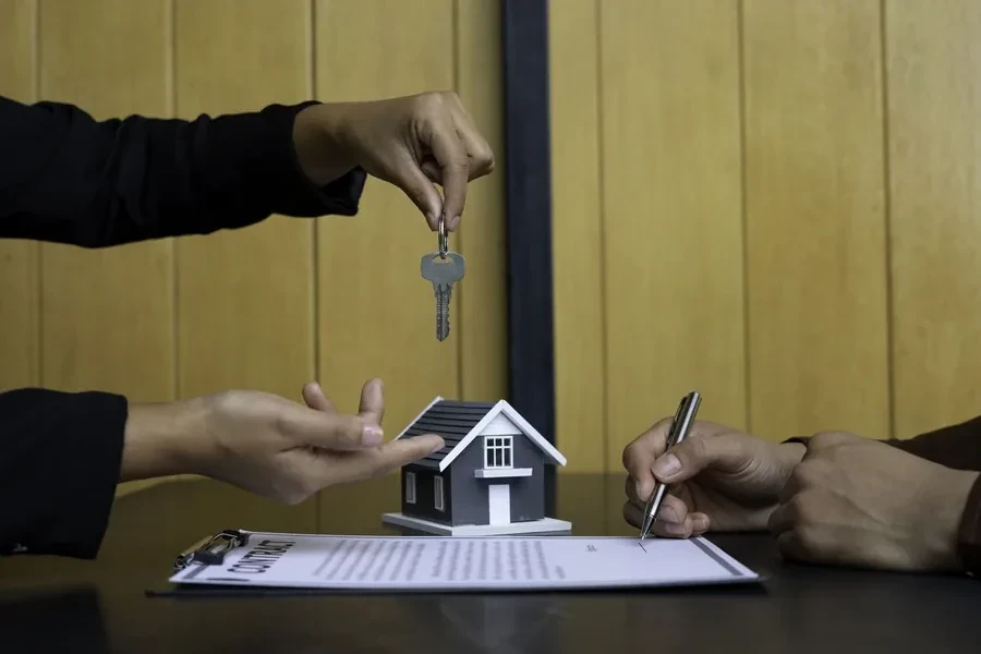 Keys handed across a signed contract beside a model house at a Florida closing table