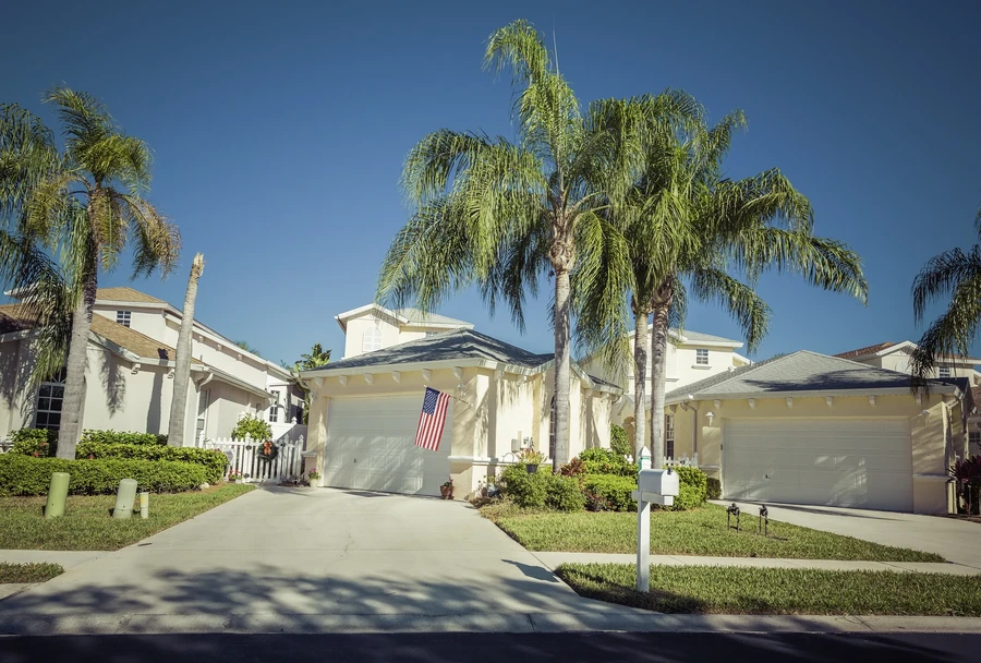 White South Florida homes with palm trees and an American flag hanging by the garage on a sunny day