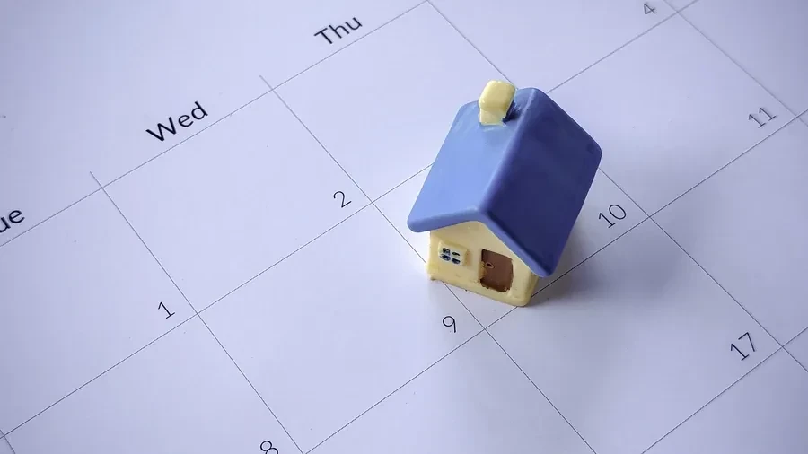 Small wooden house model beside a calendar on a blue background, representing year-end timing decisions for Florida home buyers