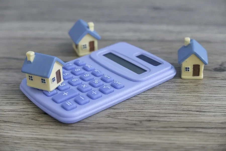 Calculator and small model houses on a wooden desk, representing the break-even math on a Florida mortgage refinance