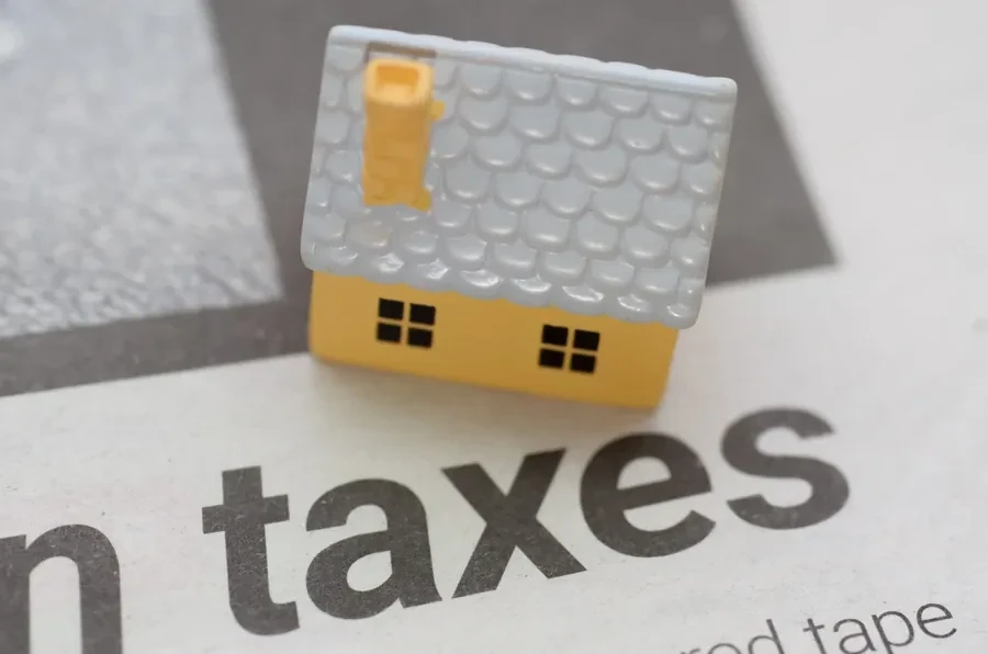 Small yellow model house beside a newspaper and red tape, representing tax returns and documentation on a self-employed Florida mortgage file