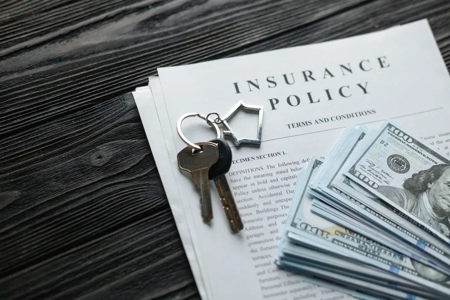 Insurance policy document with house keys and cash on a dark wood table, representing title insurance at a Florida closing